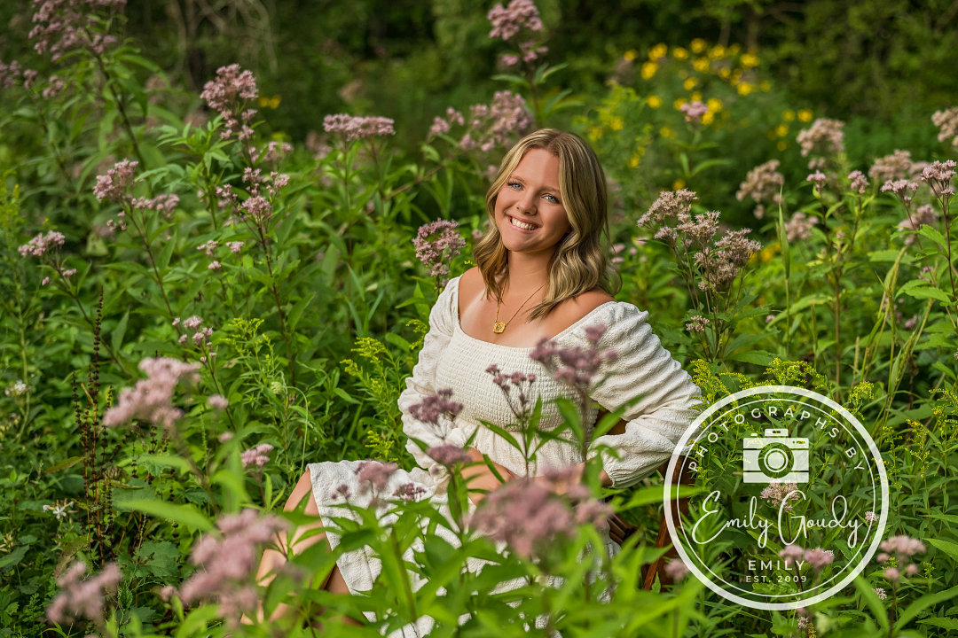 Image by Photographs by Emily, Emily Goudy, of a senior girl sitting on a chair surrounded by florals.
