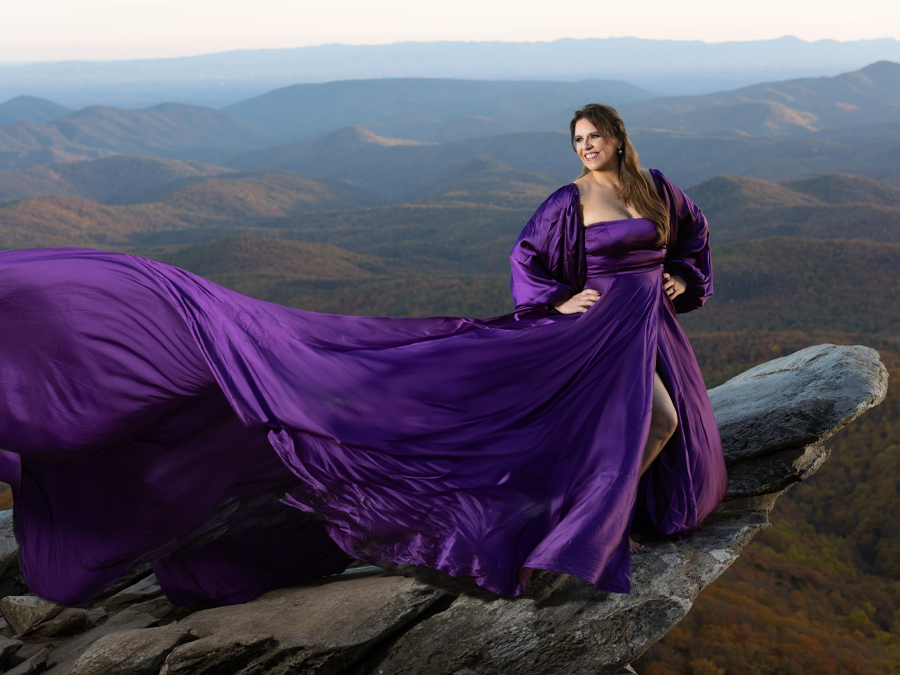 Image by Cathy Anderson Photography of a woman in a flowy purple gown standing on a rock ledge.