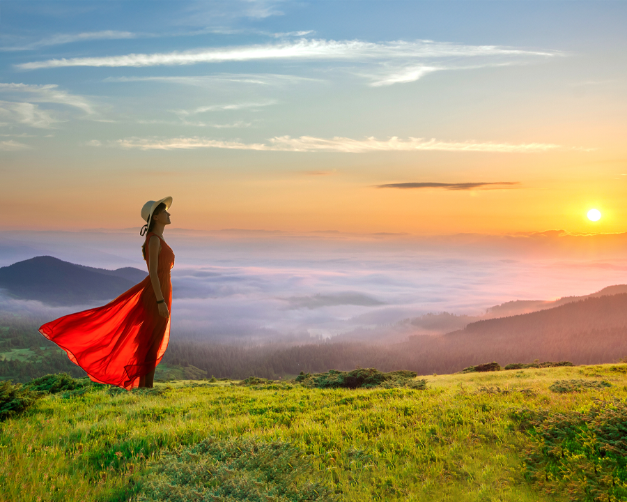 Young woman in red dress looking out over the mountains at sunrise.